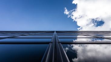 Korkean rakennuksen ikkunoiden pinnasta heijastuu sininen taivas, jolla leijailee valkoinen pilvi.