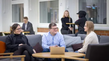 Kolme eri-ikäistä henkilöä istuu sohvalla keskustelemassa hyväntuulisesti.