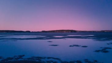 Sininen hetki talvisessa järvimaisemassa, taivaanrannassa violetinsävyinen auringonlasku.