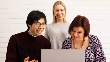 Kolme henkilöä katselee kannettavan tietokoneen näyttöä hymyillen.