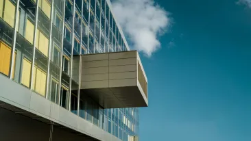 Kerrostalon ikkunoiden heijastavasta pinnasta ulkonee katettu parveke sinistä taivasta vasten.