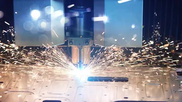 Lähikuva metallilevyn laserleikkauksesta, jossa kipinät sinkoilevat.