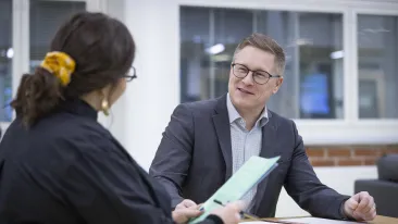 Kaksi henkilöä keskustelee iloisesti pöydä ääressä istuen.