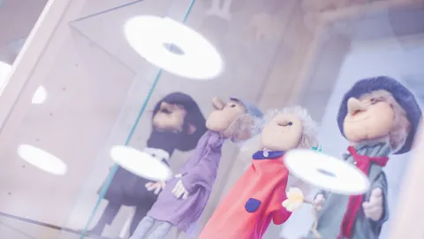 Neljä vanhaa ihmistä esittävää nukkea ovat esillä hyvin valaistussa vitriinissä.