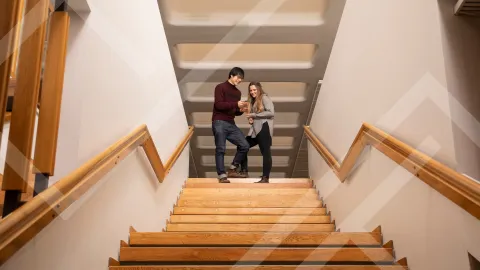 Kaksi henkilöä on pysähtynyt puisten portaiden yläpäähän katsomaan hymyillen kännykän ruutua. 